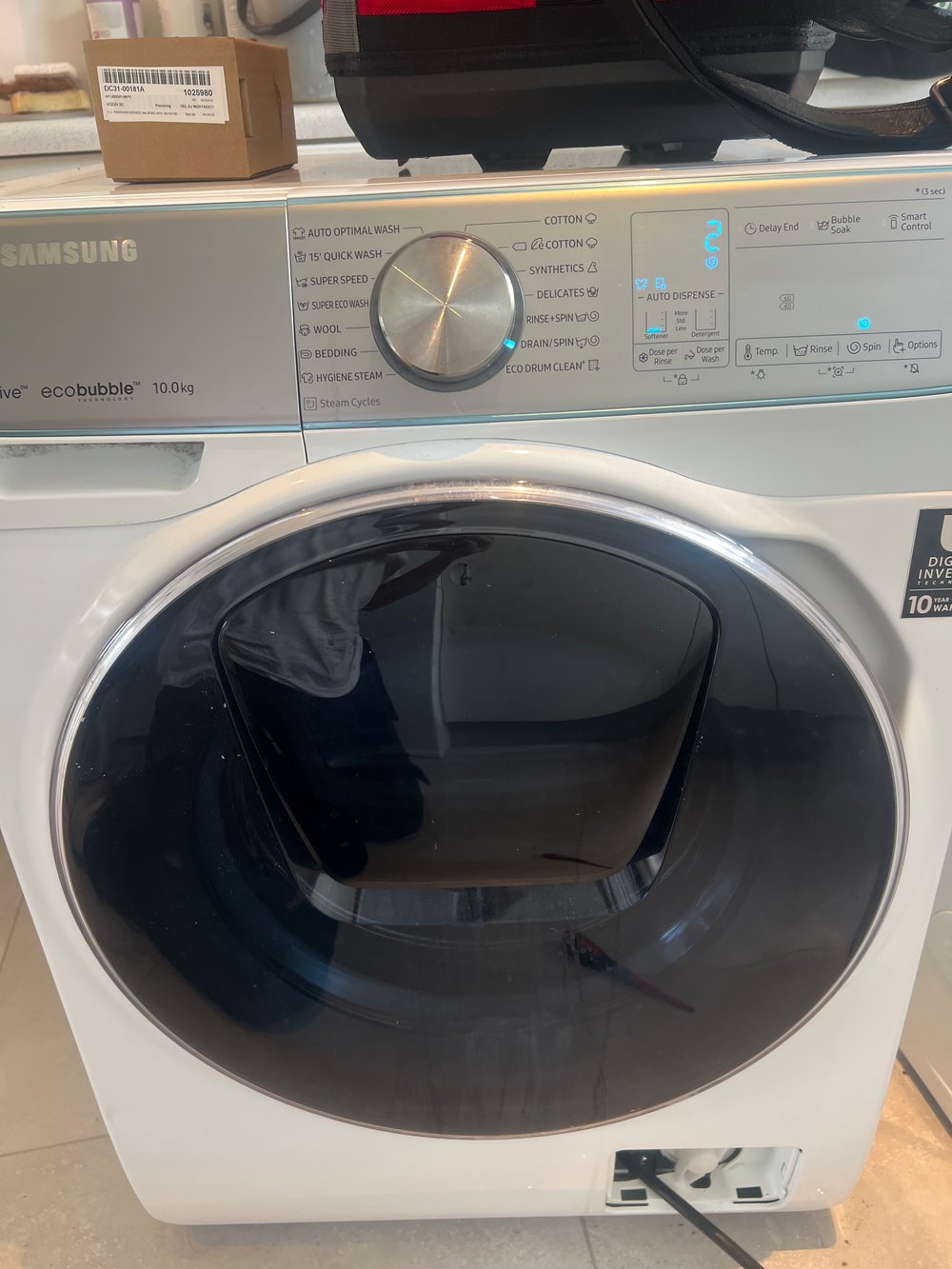 Hvid Samsung vaskemaskine under reparation med reservedel ovenpå