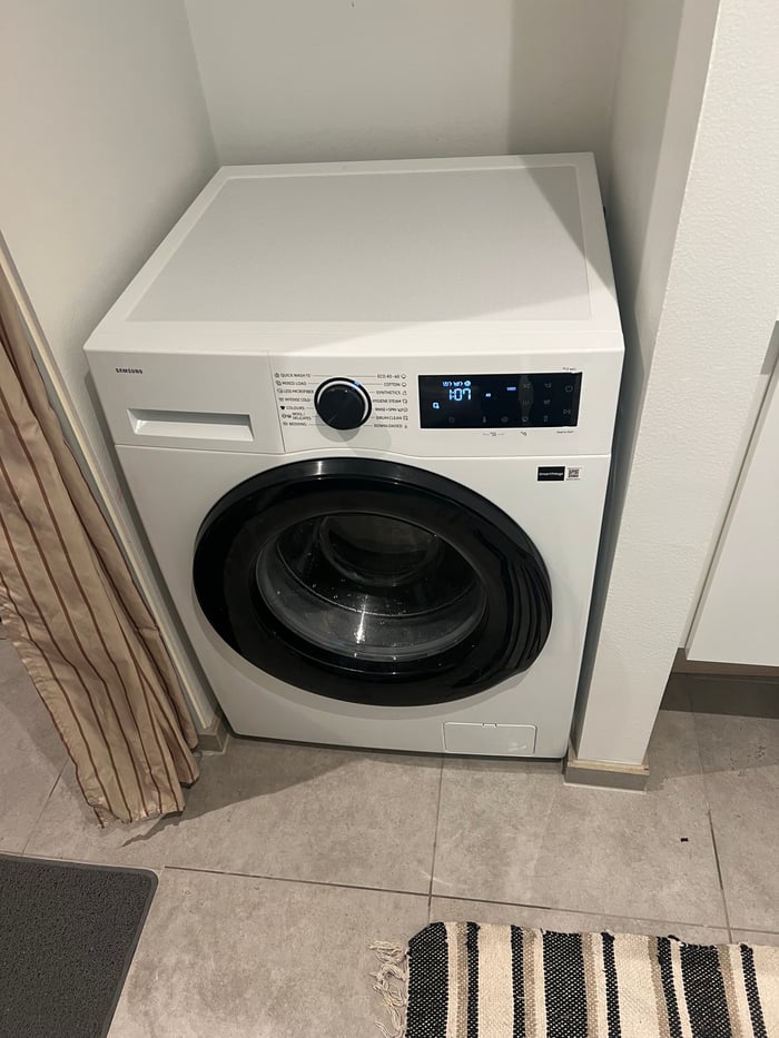 Hvid Samsung vaskemaskine installeret i en niche på gråt klinkegulv